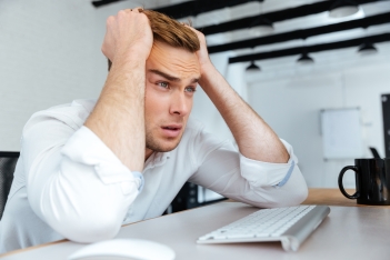 Upset disappointed young businessman sitting with hands on head
